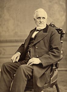 220px-John_Taylor_seated_in_chair