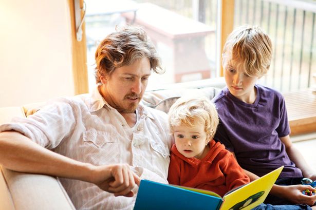 Father and sons reading book on couch